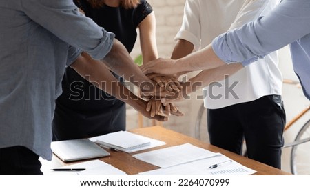 Close up group of multiracial business people colleagues joining hands together over table, strengthening team spirit, motivating at meeting, involved together in teambuilding activity in office.
