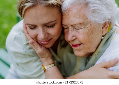 Close up of grownup granddaughter and senior grandmother cuddling, enjoying tender moment, hugging, expressing love,sittingon bench in park.