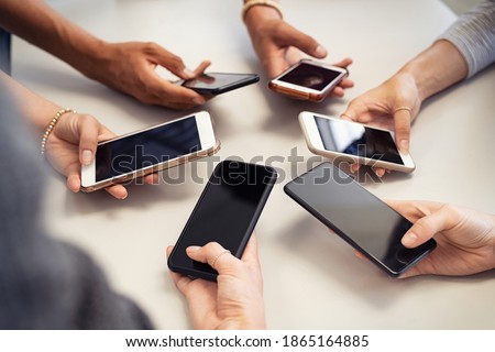 Close up of guys and girls hands in circle using smart phone. High angle view of multiple hands holding mobile phone with empty screen. Group of multi cultural friends using smartphone together.