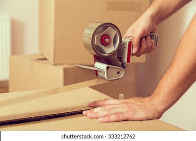 Close up of a guy's hands holding packing machine and sealing cardboard boxes with duct tape - Shutterstock ID 333212762
