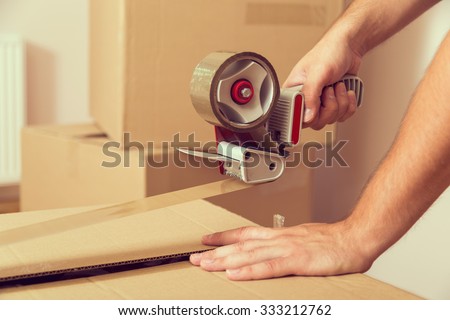 Close up of a guy's hands holding packing machine and sealing cardboard boxes with duct tape