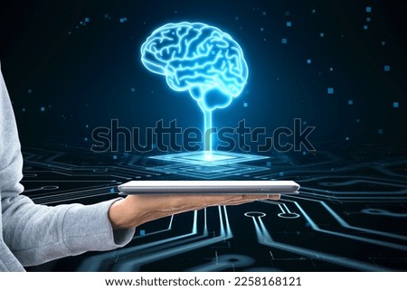 Close up of hacker hand holding tablet with glowing circuit brain hologram on dark background. AI, machine learning and futuristic technology concept