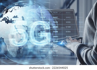 Close up of hacker hands using laptop with glowing planet earth globe hologram with 5G and index graph on blurry interior background. Mobile internet network, speed and signal. Double exposure