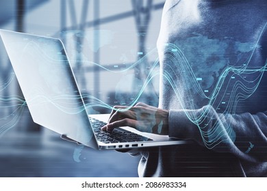 Close up of hacker using laptop in blurry office interior with creative glowing business chart and map hologram on blurry background. Business data, hacking and market concept. Double exposure