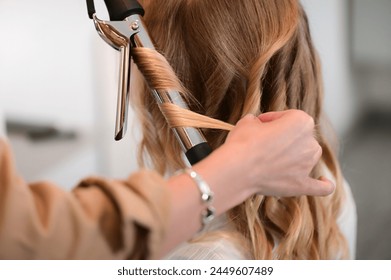 Close up of hairdresser using hot iron or hair straightener for curly hair of a blonde client - Powered by Shutterstock