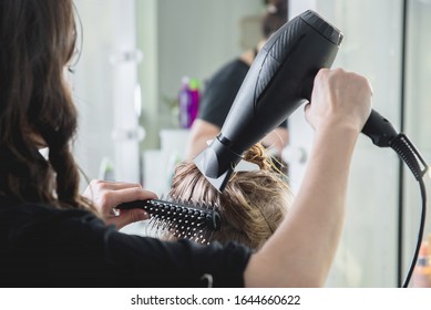Close up of hairdressers hands drying long blond hair with blow dryer and round brush