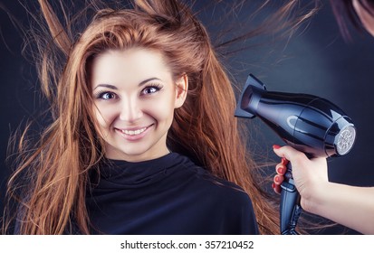 Close up of hairdressers hands drying long hair with blow dryer on a dark background