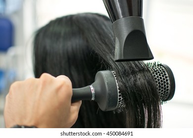 Close Up Of Hairdressers Hands Drying Long Black Hair With Blow Dryer And Round Brush.