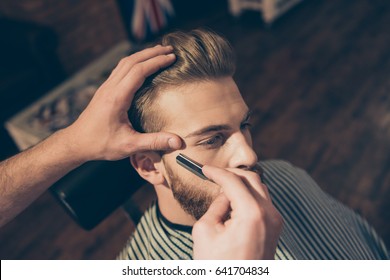 Nahaufnahme eines Friseurwerkes für einen attraktiven jungen Blond im Friseur. Er stylt seinen Bart und rasiert ihn mit geraden Rasierapparaten