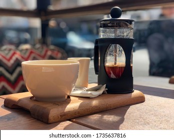 Close Up Of A Half Full Coffee French Press With White Porcelain Mug And Milk Saucer On A Wooden Board At A Street Coffee With Shallow Depth Of Field