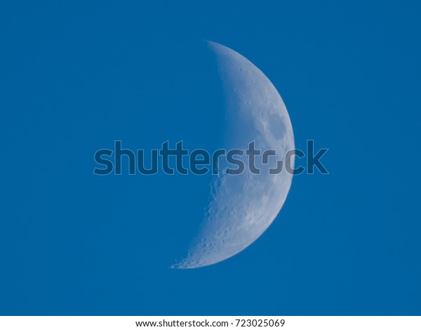 Close up half moon on daytime sky blue or azure\
sky background. It is a black and white image that see details on\
the surface. Look again is awesome suitable for background. Moon\
orbit planet Earth.