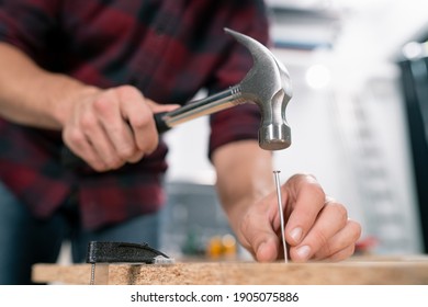 Close up of hammering a nail into board. A carpenter wearing a red flannel shirt, jeans and cloth protective gloves nails the wooden boards. - Shutterstock ID 1905075886