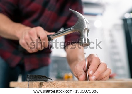 Close up of hammering a nail into board. A carpenter wearing a red flannel shirt, jeans and cloth protective gloves nails the wooden boards. Foto d'archivio © 