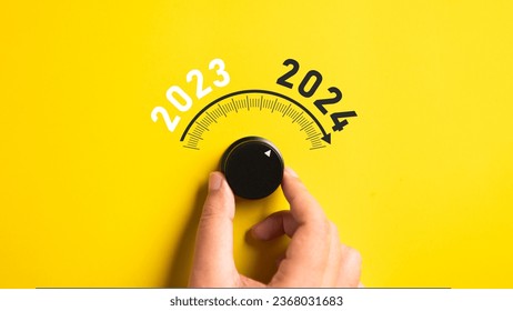 Close up of a hand adjusting volume button from year 2023 to 2024 on isolated yellow background. Happy New Year celebration concept.