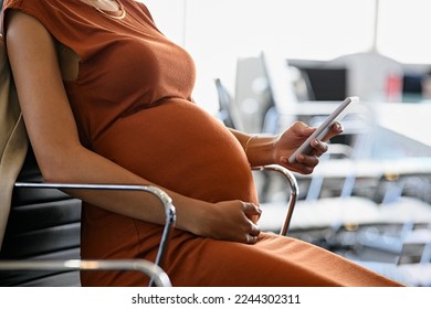 Close up hand of african pregnant woman holding belly while using smartphone in office. Pregnant businesswoman writing email on mobile phone while working. Expecting woman reading text message on cell - Powered by Shutterstock