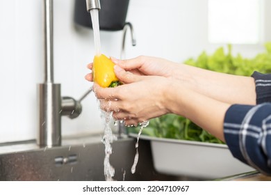 Close up hand of asian young housekeeper woman, washing sweet pepper, yellow paprika, vegetables with splash water in basin of water on sink in kitchen, preparing fresh salad, cooking meal.Health food