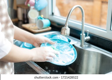 Close up hand of attractive young Asian woman is washing dishes at kitchen sink while doing cleaning at home during Staying at home using free time about their daily housekeeping routine.