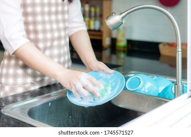 Close Up Hand Of Attractive Young Asian Woman Is Washing Dishes At Kitchen Sink While Doing Cleaning At Home During Staying At Home Using Free Time About Their Daily Housekeeping Routine.
