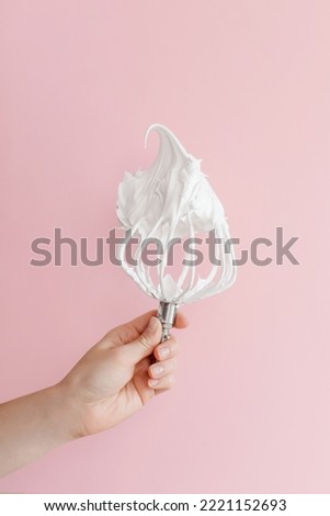 Close up of a hand balloon whisk with beaten egg white raw meringue for perfect peaks on pink background. High quality photo