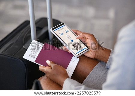Close up hand of black businesswoman checking flight eticket on phone while holding passport and boarding pass. African american woman hand checking online travel plane ticket on mobile phone.