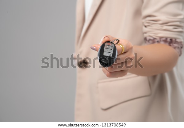 Close up hand of business woman\
holding smart key on grey background. Immobilizer car\
key.