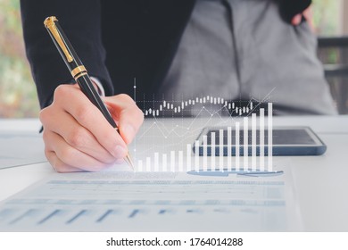 Close up hand businessman writing with pen, financial data and sales rates and market exchanges or appropriate paper reports with graphs showing business growth. Concepts of financial investment - Shutterstock ID 1764014288