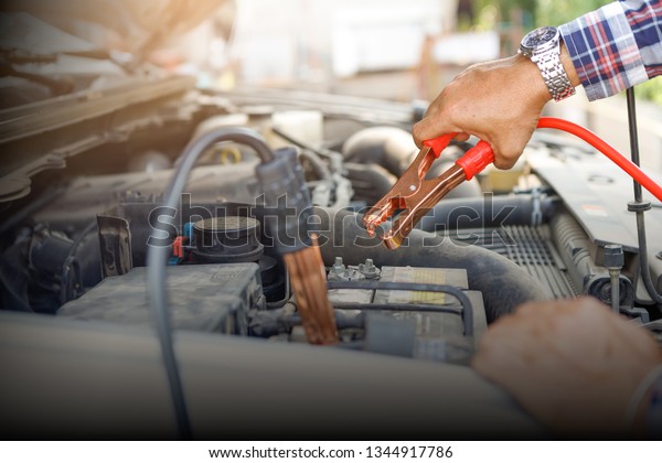 Close up hand of car technician holding cable to\
connect to battery,Car mechanic uses battery jumper cable charge a\
dead battery,A car mechanic uses battery jumper cable transferring\
power,spot focus.