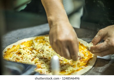 Close Up Hand Of Chef Sprinkles Cheese On The Pizza In Kitchen, (Visible Noise Due To High ISO, Soft Focus)