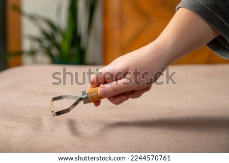 Close up of hand cleaning sofa surface with a carpet scraper tool. Rug cleaning device.