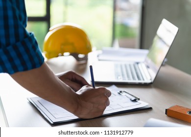 Close Up Hand Of Construction Worker Or Designer Reviewing Construction Blueprint Or Drawing On Table At Construction Site Or Office.