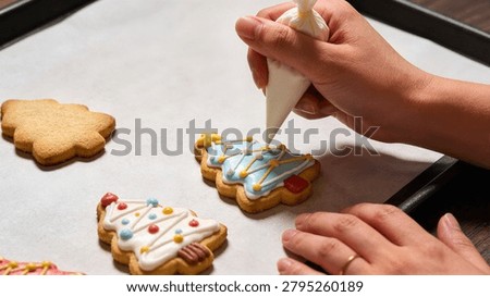 Close up of hand decorating Christmas tree shaped sugar cookies with blue royal icing perfect for holiday baking advertisement and recipe promotion