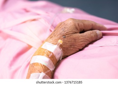 Close Up Hand Of Elderly Over 80 S Asian Man Patient With Intravenous Catheter For Injection Plug, Saline Transfusion Or Brine Drip During The Chemotherapy Of Liver Cancer In Hospital Ward Room

