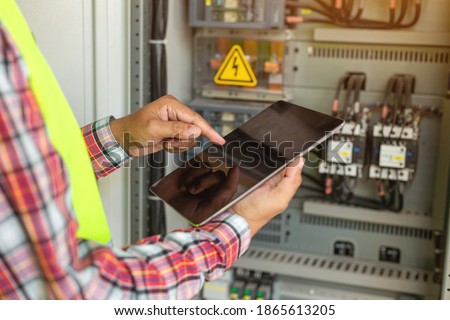 Close up hand of engineer or electrician man working check the electrical system with tablet at factory. 