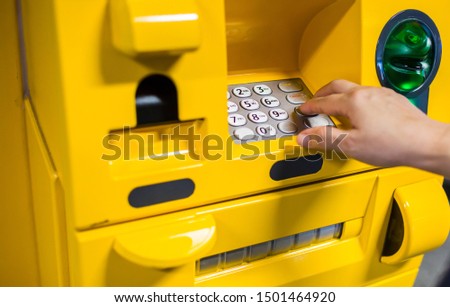 Close up of hand entering pin at an yellow ATM. Finger about to press a pin code on a pad. Security code on an yellow automated teller machine (ATM).  ATM entering pin. Selective focus.