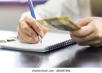Close up hand female with pencil writing on the book and hand hold US dollar. Calculation at home - Shutterstock ID 682687606