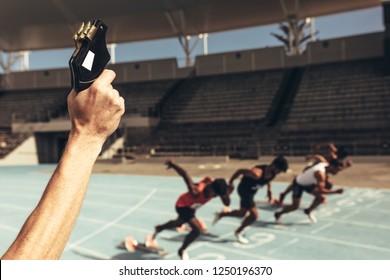 Close Up Of Hand Firing A Starter Pistol To Start The Running Race. Athletes Starting Off For A Race On A Running Track.