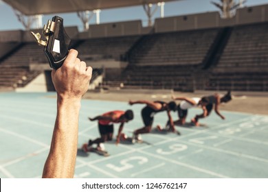 Close Up Of Hand Firing A Starting Pistol To Start A Race. Athletes Taking Off From Starting Block On A Running Track At The Start Of A Race.