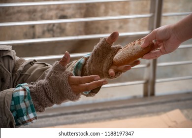 Close Up Hand Forwarding Bread To Starving Beggar. Close Up Hand Sharing Food For Homeless. Close Up Dirty Hands Of Poor People Wearing Knitting Glove, Receiving Bun From Kind People. Sharing Concept.