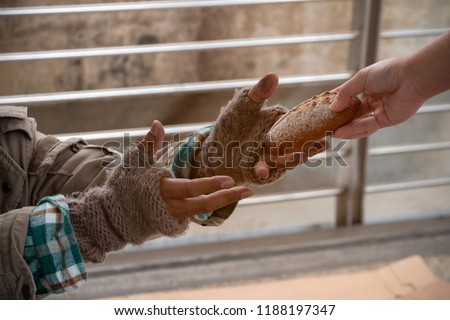 Close up hand forwarding bread to starving beggar. Close up hand sharing food for homeless. Close up dirty hands of poor people wearing knitting glove, receiving bun from kind people. Sharing concept.
