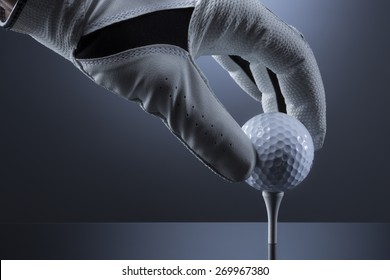 Close Up Of Hand  With Golf Glove Putting Ball On Tee, Isolated On Dark Blue Background.