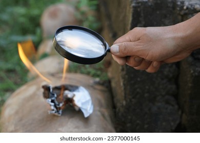 Close up hand hold magnifying glass to make fire for burning paper. Concept, Science experiment about convex lens, hold magnifying glass between the sun and tinder. Handy survival skill              