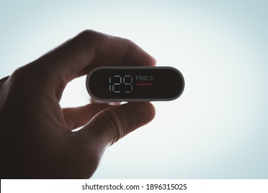 Close Up Hand Holding Air Quality Monitor To Detect Level Of Pollution Or Small Particle (PM2.5) On Sky Background. Image High Pollution Concept.