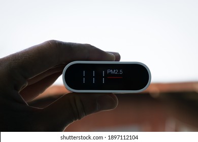 Close Up Hand Holding Air Quality Monitor To Detect Level Of Pollution Or Small Particle (PM2.5) On Home Background. Image High Pollution Concept, More Than 100.