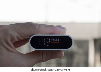 Close Up Hand Holding Air Quality Monitor To Detect Level Of Pollution Or Small Particle (PM2.5) On Home Background. Image High Pollution Concept.