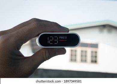 Close Up Hand Holding Air Quality Monitor To Detect Level Of Pollution Or Small Particle (PM2.5) On Home Background. Image High Pollution Concept.