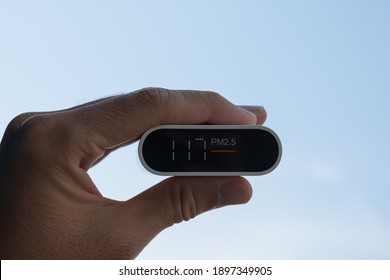 Close Up Hand Holding Air Quality Monitor To Detect Level Of Pollution Or Small Particle (PM2.5) On Sky Background. Image High Pollution Concept.