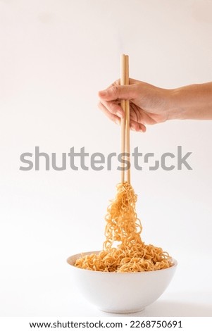 Close up hand holding the bamboo chopsticks over instant noodles isolated on white background. 
