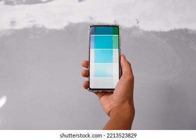 Close Up Of Hand Holding Cellphone With Digital Paint Swatch Against Grey Wall