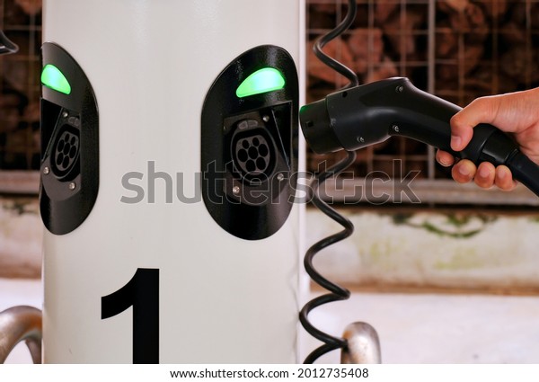 Close up of hand holding charging device,\
plugging into charging point station of car sharing electric\
vehicle in multi-storey\
carpark