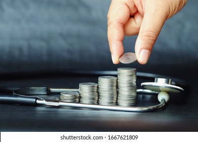 Close Up Hand Holding Coin, Stack Of Money And Stethoscope On Black Background, Saving And Manage For Healthy, Medical And Healthcare, Life Insurance Business Technology Concept